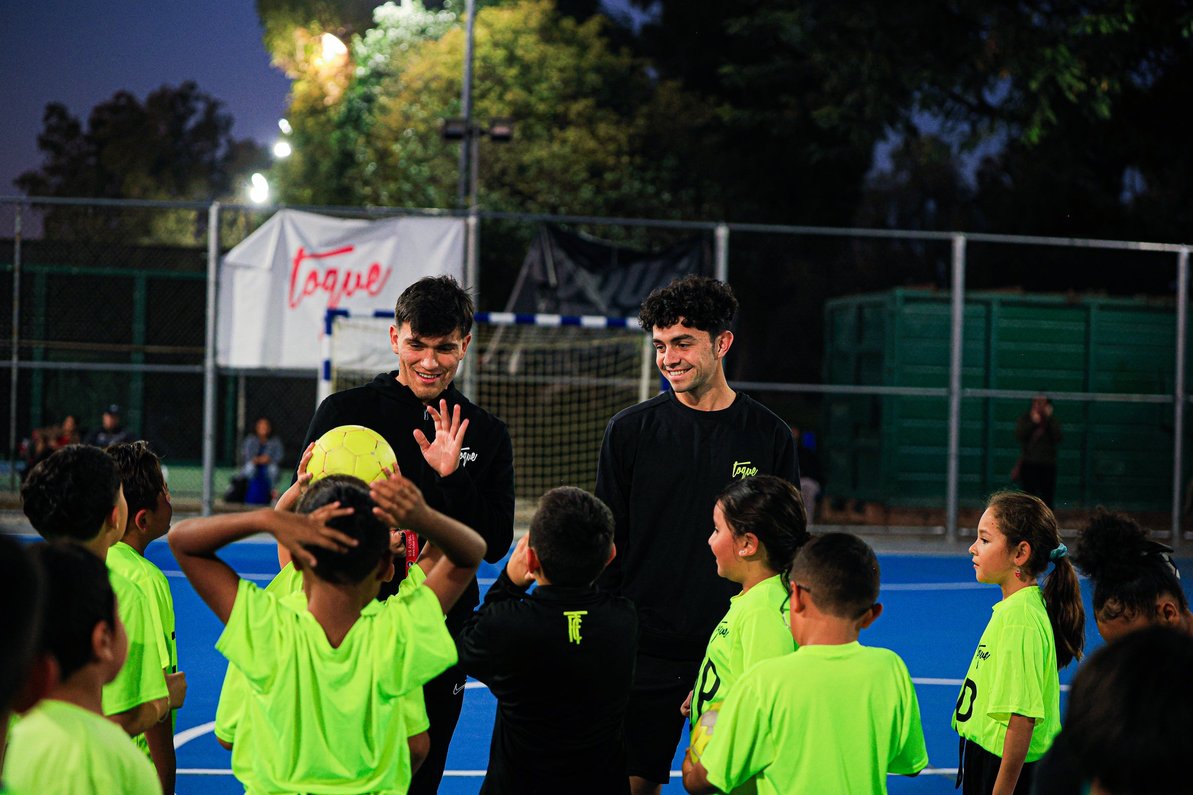Children in bright green Toque jerseys with a coach on a sports field at night.