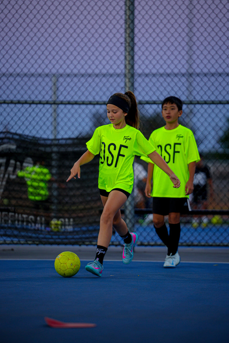 Two children in Toque bright green jerseys playing on a sports court.